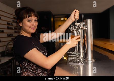 Porträt der Kellnerin im Profil, die ein Glas Bier aus dem Zapfhahn füllt. Stockfoto