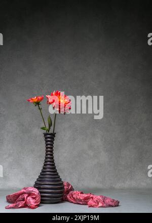 Stillleben mit Dahlien. Zwei rote Dahlien in einer dunklen Vase auf dunklem Hintergrund. Kopierbereich Stockfoto