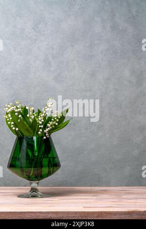 Weiße Blumen, Maiglöckchen in einer grünen, transparenten Vase. Grauer Hintergrund. Viel Platz für Text. Stockfoto