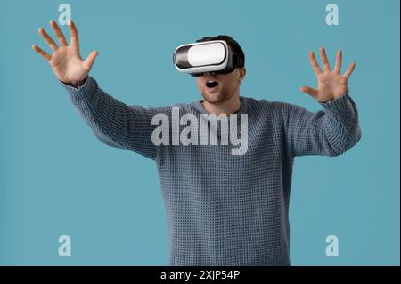 Schöner junger Mann, der den virtuellen Bildschirm in einer Virtual-Reality-Brille auf blauem Hintergrund berührt Stockfoto