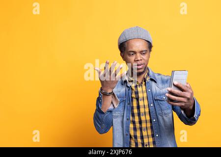 afroamerikaner Carefree Guy überprüft seine Smartphone-Benachrichtigungen auf der Kamera, surft online auf Webseiten und Social-Media-Apps. Selbstbewusster Gelegenheitsmensch spricht mit seinen Freunden über eine Internetverbindung. Stockfoto
