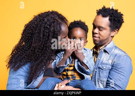 Liebevolle afroamerikaner-Mutter und Vater küssen ihr kleines Kind im Studio und fühlen sich dankbar für die kleine Familie, die sie haben. Junge Eltern umarmen ihren kleinen Jungen vor der Kamera. Stockfoto