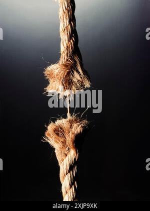 Ein Nahbild eines ausgefransten Seils, das vor dunklem Hintergrund hängt. Stockfoto