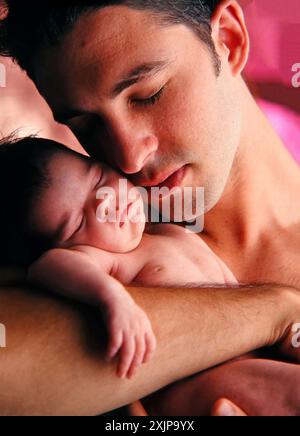 Ein Vater hält sein neugeborenes Baby, das friedlich in seinen Armen schläft. Die Augen des Vaters sind geschlossen, und er hat einen sanften Gesichtsausdruck wie h Stockfoto
