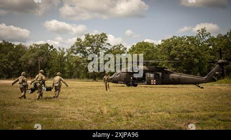 Soldaten des 224. Brigade Ingenieur-Bataillons, 2. Brigade Combat Team, 34. Infanteriedivision, Iowa Army National Guard, tragen einen Soldaten mit simulierten Verletzungen auf einem Wurf, der mit einem UH-60 Black Hawk Hubschrauber evakuiert wird, der von Soldaten der Kompanie G, 1. Bataillon, 189. Fliegerregiment, gesteuert wird. Oregon Army National Guard, während einer Massenübung im Rahmen einer XCTC-Rotation (Exportable Combat Training Capability) am 18. Juli 2024 in Camp Ripley, Minn. Während der XCTC trainieren Komponenten des 2/34sten BCT (einschließlich Infanterie, Kavallerie, Feldartillerie und Ingenieure) dynamisch und challe Stockfoto