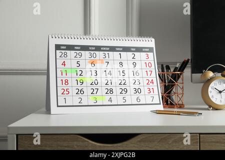 Zeitplan. Kalender mit gekennzeichneten Daten, Wecker und Schreibwaren auf weißem Tisch drinnen Stockfoto