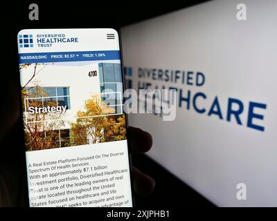 Stuttgart, Deutschland, 18.06.2023: Person, die ein Mobiltelefon hält, mit Webseite des Immobilienunternehmens Diversified Healthcare Trust auf dem Bildschirm mit Logo. Stockfoto
