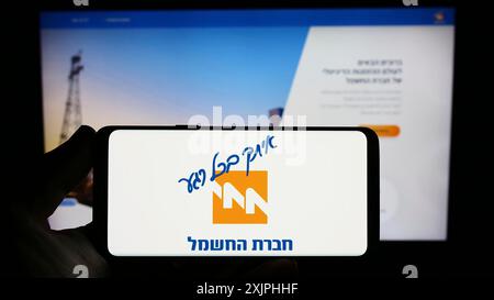 Stuttgart, 24.06.2023: Person mit Smartphone und Logo des Energieversorgers Israel Electric Corporation (IEC) vor dem Bildschirm Stockfoto