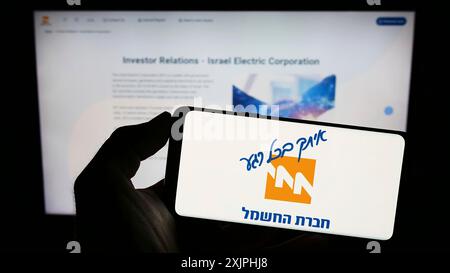 Stuttgart, 24.06.2023: Person, die ein Mobiltelefon hält, mit dem Logo des Energieversorgers Israel Electric Corporation (IEC) vor dem Bildschirm Stockfoto