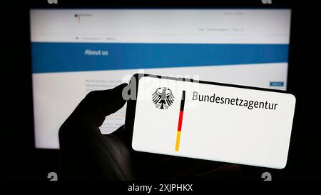 Stuttgart, 24.06.2023: Person, die ein Mobiltelefon mit dem Logo der Bundesnetzagentur (BNetzA) auf dem Bildschirm vor der Webseite hält. Stockfoto