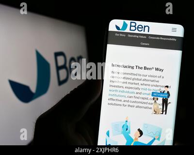 Stuttgart, 24.06.2023: Person, die ein Mobiltelefon hält, mit Webseite der Beneficient Company Group (Trustben) auf dem Bildschirm vor dem Logo. Fokus Stockfoto