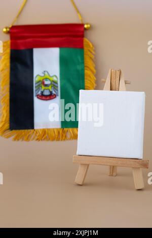 Leere weiße Pappe kleine Flagge der VAE auf beigefarbenem Hintergrund mit bunten Umschlägen. Kopierbereich. Vorlage für Werbeanzeigen vortäuschen. Reisegutschein mit dem nationalen Symbol der Vereinigten Arabischen Emirate. Besuchen Sie Dubai Concept Stockfoto