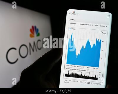 Stuttgart, 25.06.2023: Person, die ein Mobiltelefon hält, mit Webseite des US-amerikanischen Telekommunikationsunternehmens Comcast Corporation auf dem Bildschirm mit Logo. Fokus Stockfoto