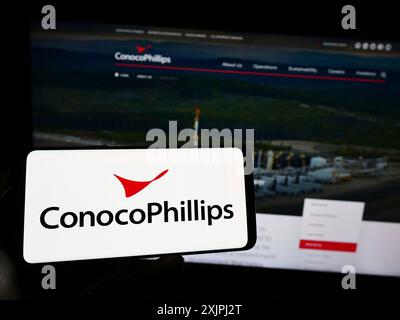 Stuttgart, 25.06.2023: Person, die ein Mobiltelefon hält, mit dem Logo des amerikanischen Öl- und Gasunternehmens ConocoPhillips Company vor dem Bildschirm Stockfoto