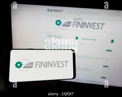 Stuttgart, Deutschland, 07.06.2023: Person mit Mobiltelefon mit Logo der italienischen Holdinggesellschaft Fininvest Spa auf dem Bildschirm vor dem Business Web Stockfoto