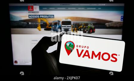 Stuttgart, Deutschland, 07.06.2023: Person mit Mobiltelefon mit Logo der brasilianischen LKW-Vermietung Grupo Vamos auf dem Bildschirm vor dem Geschäft Stockfoto