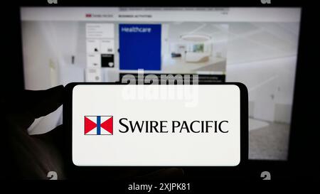 Stuttgart, Deutschland, 07-08-2023: Person, die ein Mobiltelefon mit dem Logo des asiatischen Unternehmens Swire Pacific Limited auf dem Bildschirm vor der Unternehmenswebseite hält. Stockfoto
