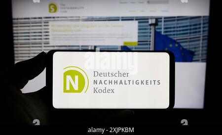 Stuttgart, Deutschland, 07.11.2023: Person, die ein Smartphone mit dem Logo des Deutschen Nachhaltigkeitskodexes (DNK) auf dem Bildschirm vor einem hält Stockfoto