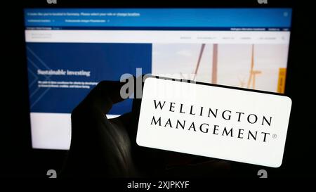 Stuttgart, 15.07.2023: Person, die ein Mobiltelefon hält, mit dem Logo der amerikanischen Wellington Management Company LLP vor dem Bildschirm Stockfoto