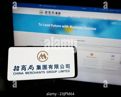 Stuttgart, 21.07.2023: Person, die ein Mobiltelefon mit dem Logo der Reederei China Merchants Group Limited auf dem Bildschirm vor der Webseite hält. Stockfoto