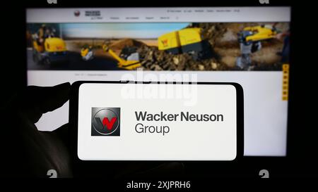 Stuttgart, 24.08.2023: Handybesitzer mit Logo des deutschen Maschinenbauunternehmens Wacker Neuson SE auf dem Bildschirm vor dem Geschäft Stockfoto