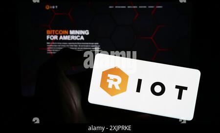 Stuttgart, 24.08.2023: Person, die ein Mobiltelefon mit dem Logo des amerikanischen Bitcoin-Bergbauunternehmens Riot Platforms Inc. Auf dem Bildschirm hält Stockfoto