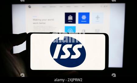 Stuttgart, Deutschland, 28.08.2023: Person, die ein Mobiltelefon mit dem Logo der dänischen Facility Management Company ISS auf dem Bildschirm vor dem Geschäft hält Stockfoto