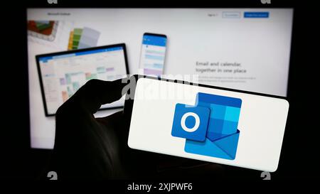 Stuttgart, Deutschland, 21.09.2023: Person, die ein Mobiltelefon mit dem Logo der E-Mail-Software Microsoft Outlook auf dem Bildschirm vor der Webseite des Unternehmens hält. Stockfoto
