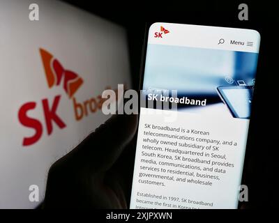 Stuttgart, 16.10.2023: Person, die ein Mobiltelefon hält, mit der Webseite des koreanischen Telekommunikationsunternehmens SK Broadband Inc. Vor dem Logo. Fokus Stockfoto