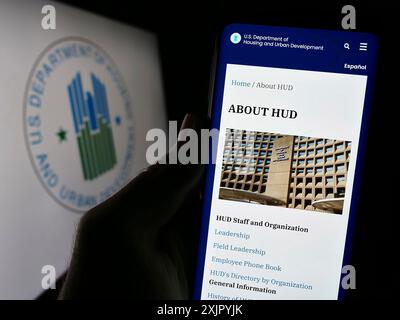 Stuttgart, Deutschland, 10-30-2023: Person, die ein Mobiltelefon hält, mit Webseite des US Department of Housing and Urban Development (HUD) vor dem Logo. Fokus Stockfoto