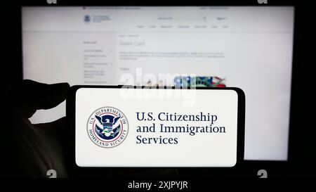 Stuttgart, 29.10.2023: Person, die ein Mobiltelefon mit dem Siegel der US-Behörde Citizenship and Immigration Services (USCIS) vor der Webseite hält. Stockfoto