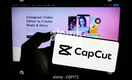 Stuttgart, Deutschland, 11.02.2023: Person, die ein Mobiltelefon mit Logo der Videobearbeitungs-App CapCut vor der Business-Webseite hält. Konzentrieren Sie sich auf das Telefon Stockfoto