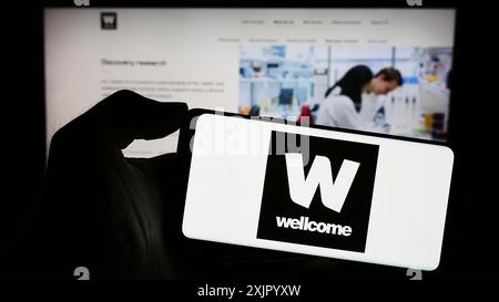 Stuttgart, Deutschland, 11.02.2023: Person mit Handy mit Logo der britischen Wohltätigkeitsstiftung Wellcome Trust vor der Webseite. Konzentrieren Sie sich auf Stockfoto