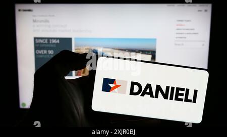 Stuttgart, Deutschland, 11.06.2023: Person, die ein Mobiltelefon mit dem Logo des italienischen Unternehmens Danieli C. Officine Meccaniche S.p.A. vor der Geschäftsstelle hält Stockfoto