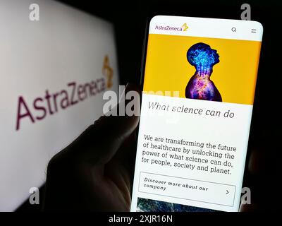 Stuttgart, 16.11.2023: Person mit Mobiltelefon und Website des Pharmaunternehmens AstraZeneca plc vor dem Firmenlogo. Fokus Stockfoto