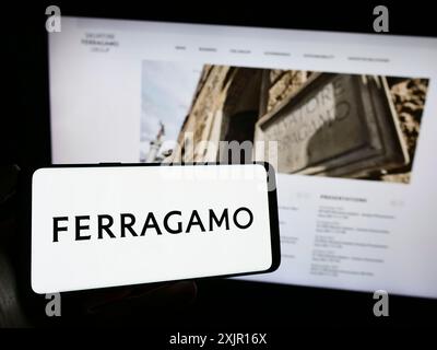 Stuttgart, 16.11.2023: Person, die ein Mobiltelefon mit Logo des italienischen Modeunternehmens Salvataore Ferragamo S.p.A. vor dem Geschäft hält Stockfoto