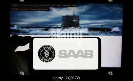 Stuttgart, 16.11.2023: Person mit Handy mit Logo des schwedischen Luft- und Raumfahrtunternehmens Saab ab ab vor der Webseite. Stockfoto