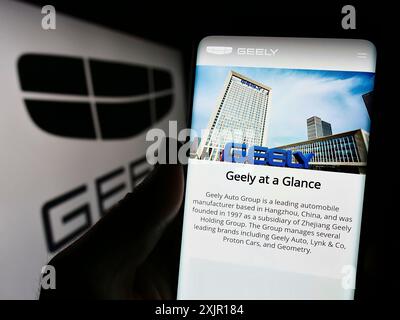 Stuttgart, 16.11.2023: Person, die ein Handy hält, mit Webseite des chinesischen Autoherstellers Zhejiang Geely Holding Group vor dem Logo. Stockfoto