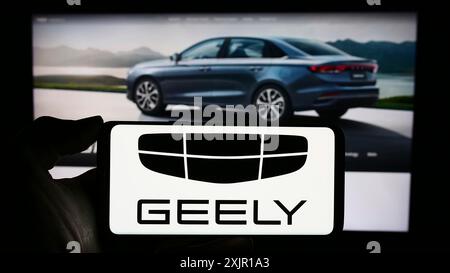 Stuttgart, 16.11.2023: Person, die ein Mobiltelefon mit dem Logo des chinesischen Autoherstellers Zhejiang Geely Holding Group vor dem Geschäft hält Stockfoto