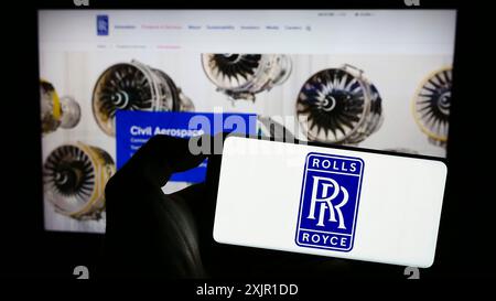 Stuttgart, 16. 11. 2023: Person, die ein Mobiltelefon mit dem Logo des britischen Luftfahrtunternehmens Rolls-Royce Holdings plc vor dem Unternehmen hält Stockfoto