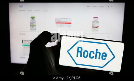 Stuttgart, 16.11.2023: Handybesitzer mit Logo des schweizerischen Gesundheitsunternehmens Roche Holding AG vor der Business-Webseite. Fokus Stockfoto