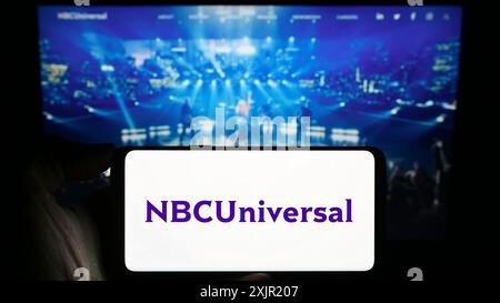 Stuttgart, 27.11.2023: Person, die ein Mobiltelefon mit Logo des amerikanischen Unterhaltungsunternehmens NBCUniversal Media LLC vor dem Unternehmen hält Stockfoto