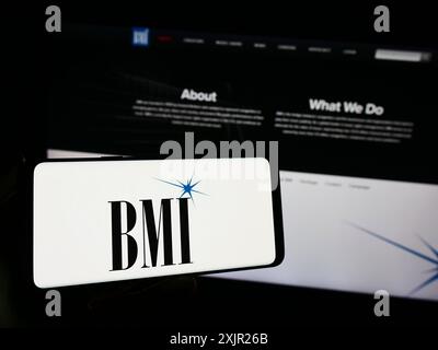 Stuttgart, 29.11.2023: Person, die ein Smartphone mit dem Logo der US-amerikanischen Firma Broadcast Music Inc. (BMI) vor der Website hält. Stockfoto