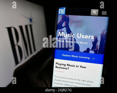 Stuttgart, Deutschland, 29.11.2023: Person, die ein Smartphone hält, mit Webseite der US-amerikanischen Firma Broadcast Music Inc. (BMI) mit Logo. Fokus Stockfoto