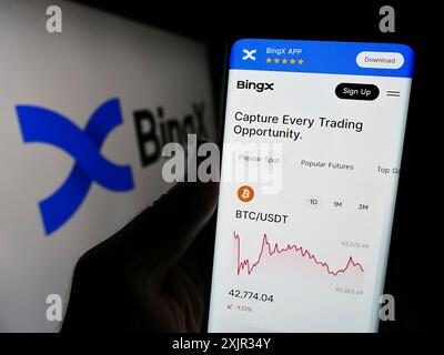 Stuttgart, 14.12.2023: Person, die ein Mobiltelefon hält, mit Webseite der Kryptowährungsbörse BingX vor dem Geschäftslogo. Konzentrieren Sie sich auf Stockfoto