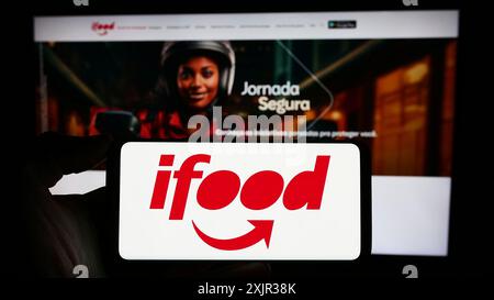 Stuttgart, Deutschland, 18.12.2023: Person mit Mobiltelefon mit Logo des brasilianischen Lebensmittelbestellungs- und Lieferunternehmens iFood vor dem Geschäft Stockfoto