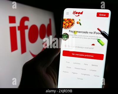 Stuttgart, Deutschland, 18.12.2023: Person, die ein Smartphone hält, mit Webseite des brasilianischen Lebensmittelbestellungs- und Lieferunternehmens iFood vor dem Logo. Fokus Stockfoto