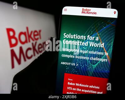 Stuttgart, 17.12.2023: Person, die ein Mobiltelefon hält, mit Webseite der US-amerikanischen Anwaltskanzlei Baker McKenzie vor dem Firmenlogo. Konzentrieren Sie sich auf die Mitte von Stockfoto