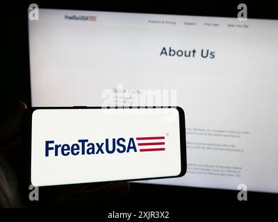 Stuttgart, 28.12.2023: Person, die ein Mobiltelefon mit dem Logo des amerikanischen Online-Steuersoftware-Unternehmens FreeTaxUSA vor dem Business Web hält Stockfoto