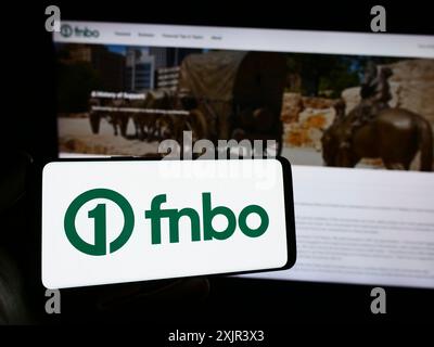 Stuttgart, 28.12.2023: Person, die ein Smartphone mit dem Logo des US-amerikanischen Finanzunternehmens First National Bank Omaha (FNBO) vor der Website hält. Stockfoto